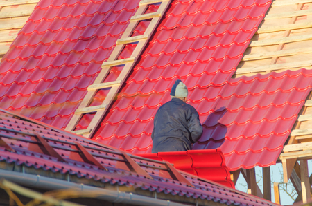 the man, the worker, the roofer covers a roof of the wooden, frame house with red metal tile, by means of the screwdriverの写真素材