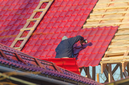 the man, the worker, the roofer covers a roof of the wooden, frame house with red metal tile, by means of the screwdriverの写真素材
