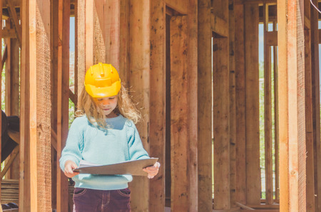 a child, a girl in a helmet on the construction site of a wooden frame house with a drawing, a drawing of the house in his handsの写真素材