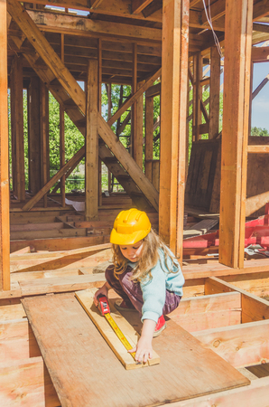 a child, a girl in a helmet on the construction of a wooden frame house with a tape measure in her handsの写真素材