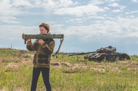Sunny day girl in uniform with a Bazooka on the background of a broken tank on the battlefield