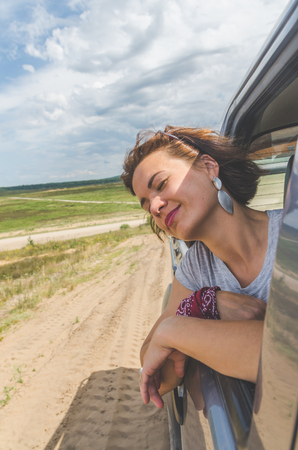 beautiful girl on an SUV in a field on a sandy road on a summer dayの写真素材