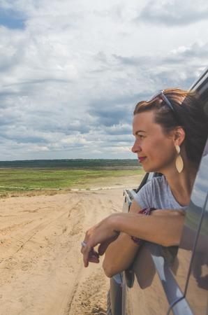 beautiful girl on an SUV in a field on a sandy road on a summer dayの写真素材