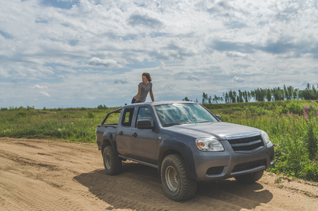 beautiful girl on an SUV in a field on a sandy road on a summer dayの写真素材