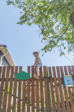a child, a girl climbs a wooden fence in the villageの写真素材