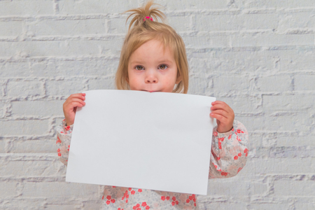 baby girl with paper sheet for CopySpace on white brick wall backgroundの写真素材