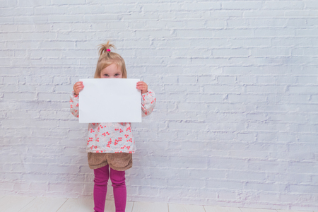 baby girl with paper sheet for CopySpace on white brick wall backgroundの写真素材