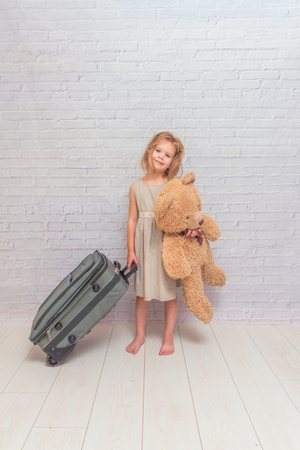 girl, baby in dress on white brick wall background with suitcase, toy bearの写真素材