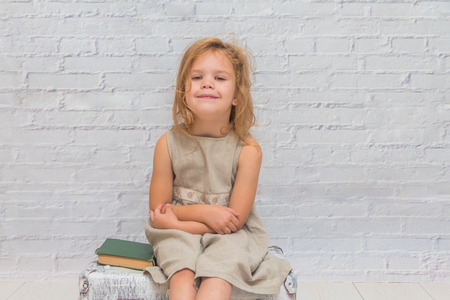 girl, baby in dress on white brick wall background with suitcase, with a book in handの写真素材
