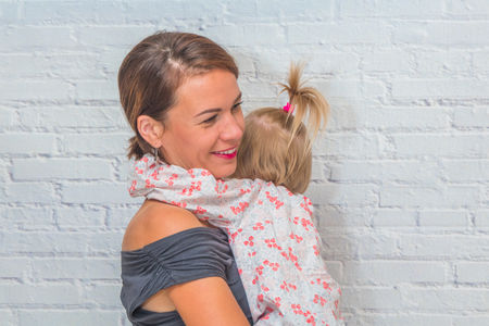 mother and daughter in her arms against a white brick wallの写真素材