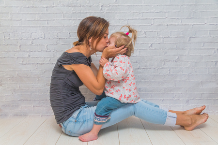 the girl, the mother and child in front of a white brick wall playing Patty-cake and kissの写真素材