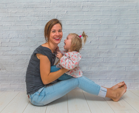 the girl, the mother and child in front of a white brick wall playing Patty-cake and kissの写真素材