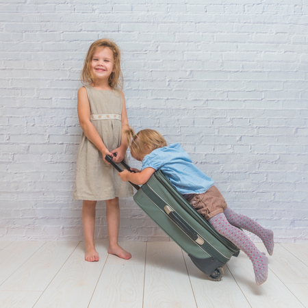 a two girls, kids with suitcase on wheels on white brick wall backgroundの写真素材