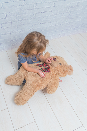 the girl, child treats a toy bear, a pill in front of a white brick wallの写真素材
