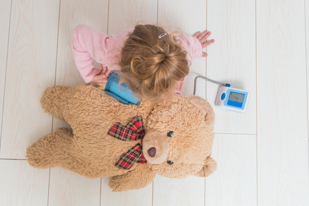 girl, a child playing doctor, measures the pressure of a bear toyの写真素材