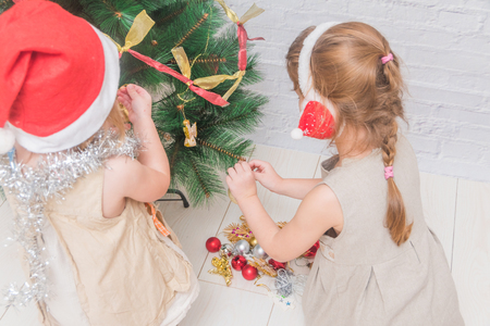 the girl, child decorates Christmas tree on white brick wall backgroundの写真素材