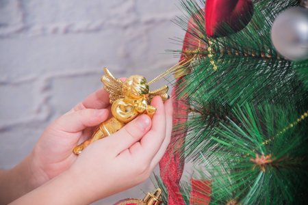 the girl, child decorates Christmas tree on white brick wall backgroundの写真素材