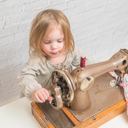 child working behind vintage sewing machine, on brick wall background