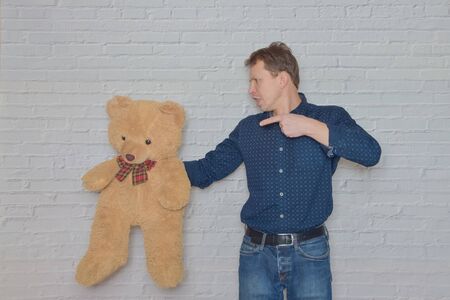 the man in a shirt gestures to the wall of white brick toy bearの写真素材