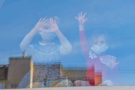the child sits at the window in a medical mask and looks out the windowの写真素材