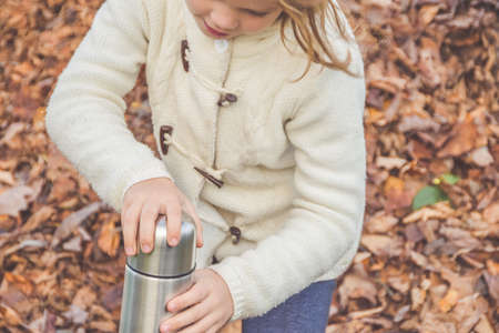 A child with a insulated bottle on fallen leavesの写真素材
