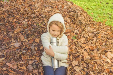 A child with a insulated bottle on fallen leavesの写真素材