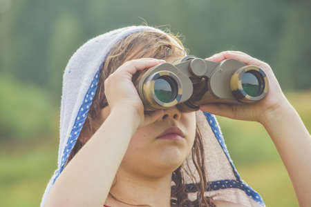 the child girl stands in a meadow and looks through binocularsの写真素材