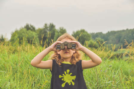 the child girl stands in a meadow and looks through binocularsの写真素材
