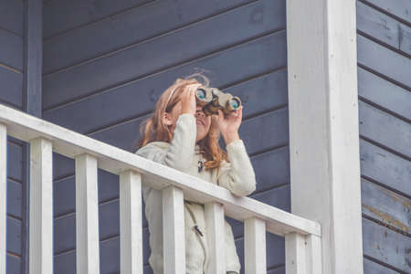 a child girl looks through binoculars standing on the balcony of the houseの写真素材