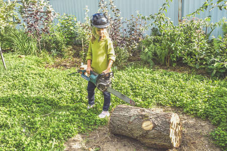 a girl child in a helmet with an electric saw saws a logの写真素材