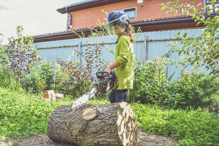 a girl child in a helmet with an electric saw saws a logの写真素材