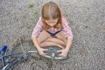 a child girl has damaged a bicycle wheel and is making repairs photo without processingの写真素材