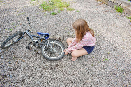 a child girl has damaged a bicycle wheel and is making repairs photo without processingの写真素材