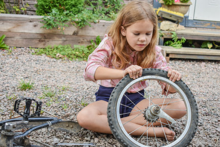 a child girl has damaged a bicycle wheel and is making repairs photo without processingの写真素材