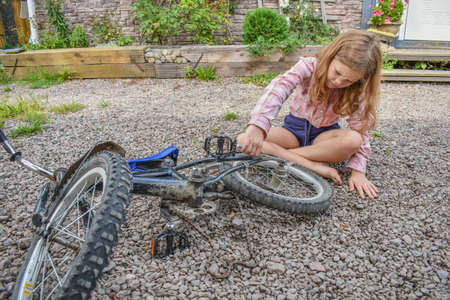 a child girl has damaged a bicycle wheel and is making repairs photo without processingの写真素材