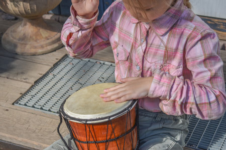 a girl child with a djembe drum outdoor on the porch of the house photo without processingの写真素材