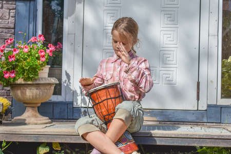 a girl child with a djembe drum outdoor on the porch of the house photo without processingの写真素材