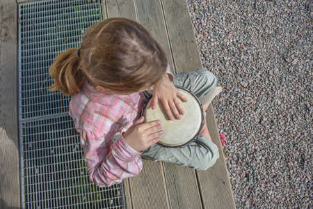 a girl child with a djembe drum outdoor on the porch of the house photo without processingの写真素材