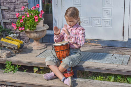 a girl child with a djembe drum outdoor on the porch of the house photo without processingの写真素材
