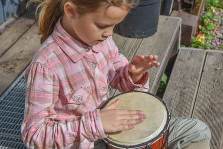 a girl child with a djembe drum outdoor on the porch of the house photo without processingの写真素材