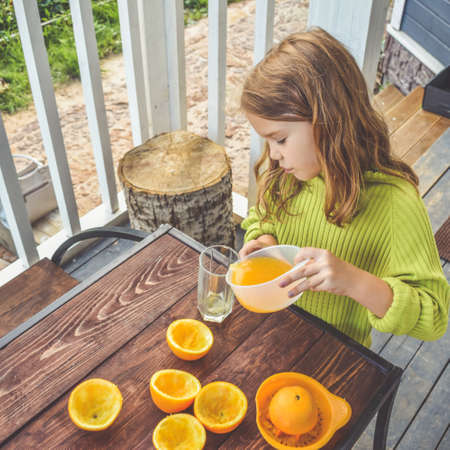 a girl child makes freshly squeezed orange juice on a manual juicerの写真素材