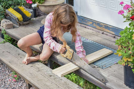 a child girl with a hacksaw saws a board outside photo without processingの写真素材