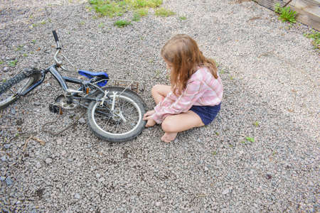 a child girl with a hacksaw saws a board outside photo without processingの写真素材