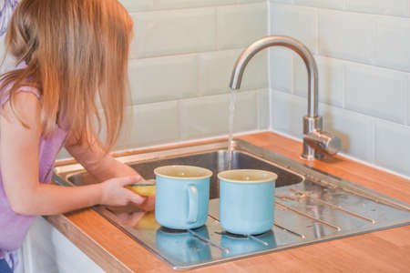 a child washes mugs in the sink photo without a filterの写真素材