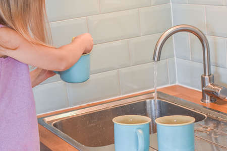 a child washes mugs in the sink photo without a filterの写真素材