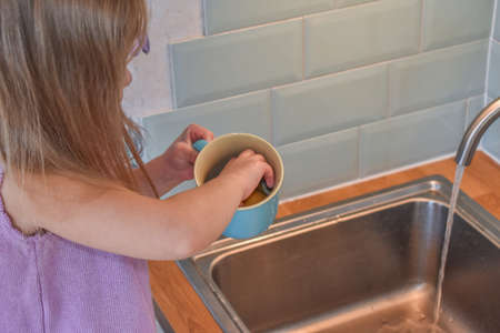 a child washes mugs in the sink photo without a filterの写真素材