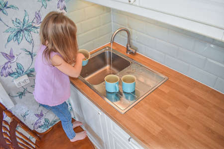 a child washes mugs in the sink photo without a filterの写真素材