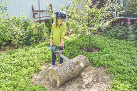 a girl child in a helmet with an electric saw saws a logの写真素材
