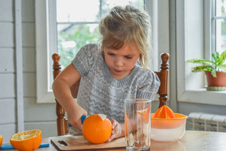 a child girl in the kitchen cuts and squeezes oranges juiceの写真素材