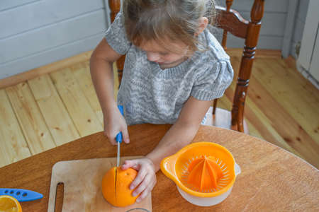 a child girl in the kitchen cuts and squeezes oranges juiceの写真素材